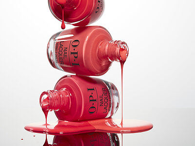 Gestapelte OPI-Nagellackflaschen tropfen rosa und roten Lack auf spiegelnde Fläche